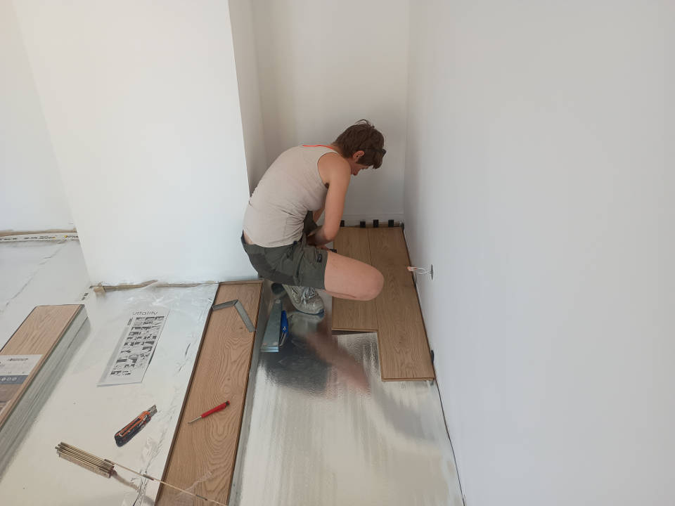 Premières lames de parquet flottant posées dans un angle de la pièce avec cales de dilatation
