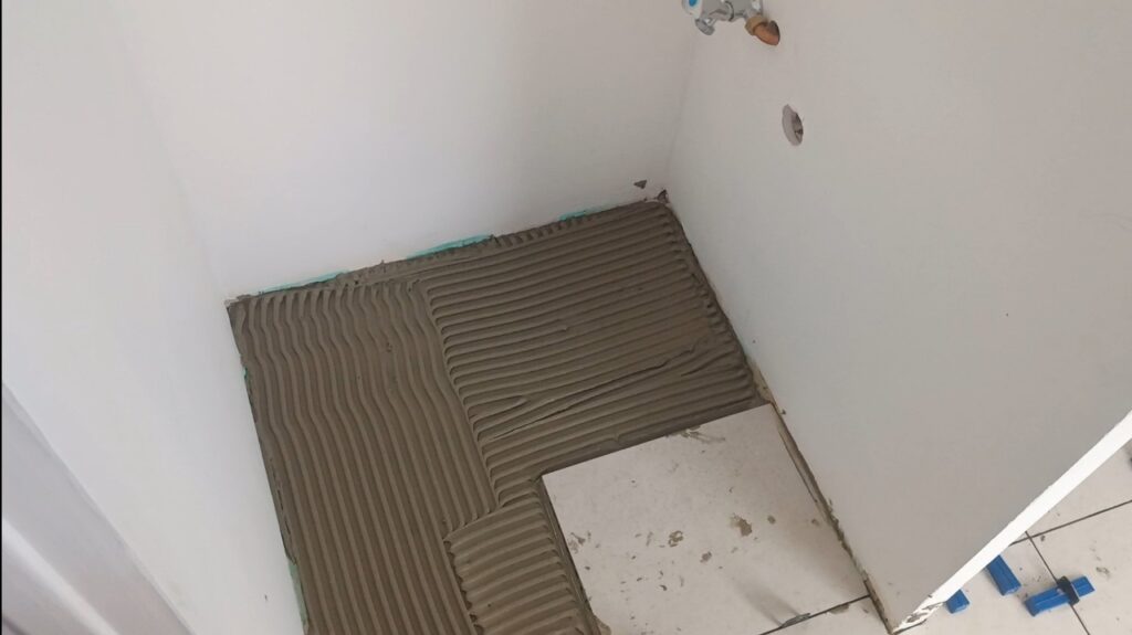 Application de la colle FlexOpen avec un peigne à colle avant la pose d’un carrelage rectifié 30x60.