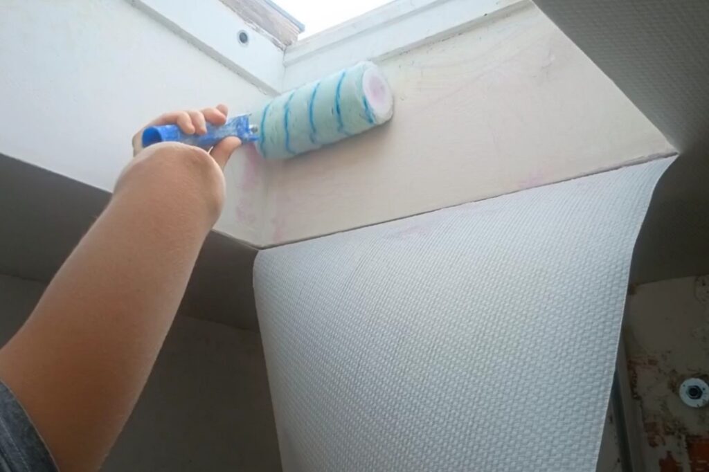 Application de colle au rouleau sur un plafond en plaques de plâtre avant la pose de la toile fibrée