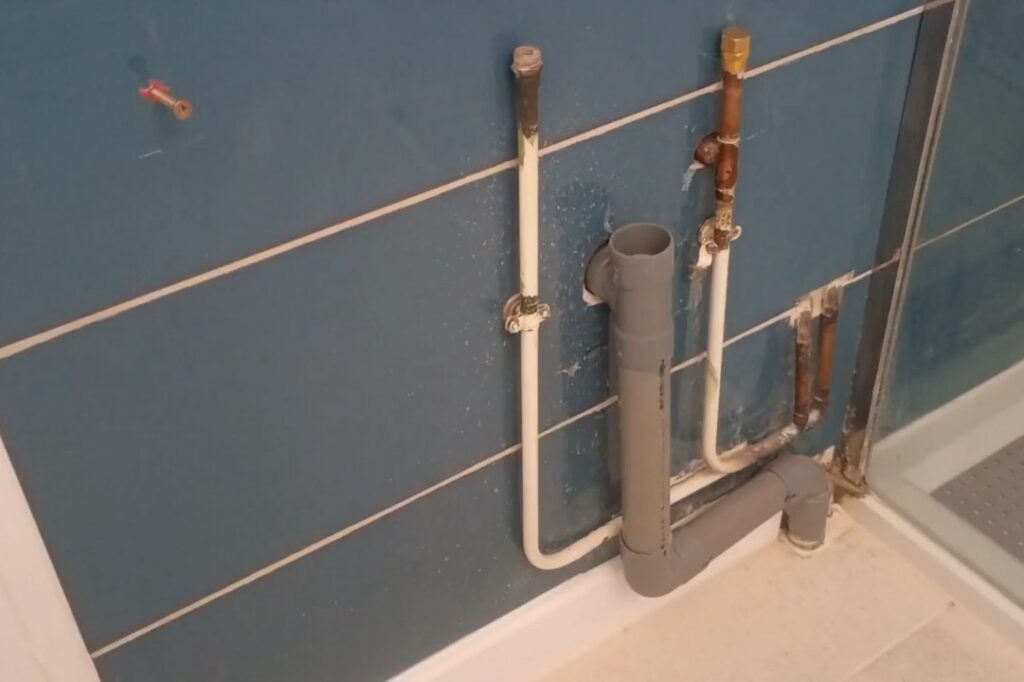 Installation terminée d’un tuyau PVC et d’une robinetterie en cuivre après perçage mural pour le raccordement d’une machine à laver en salle de bain