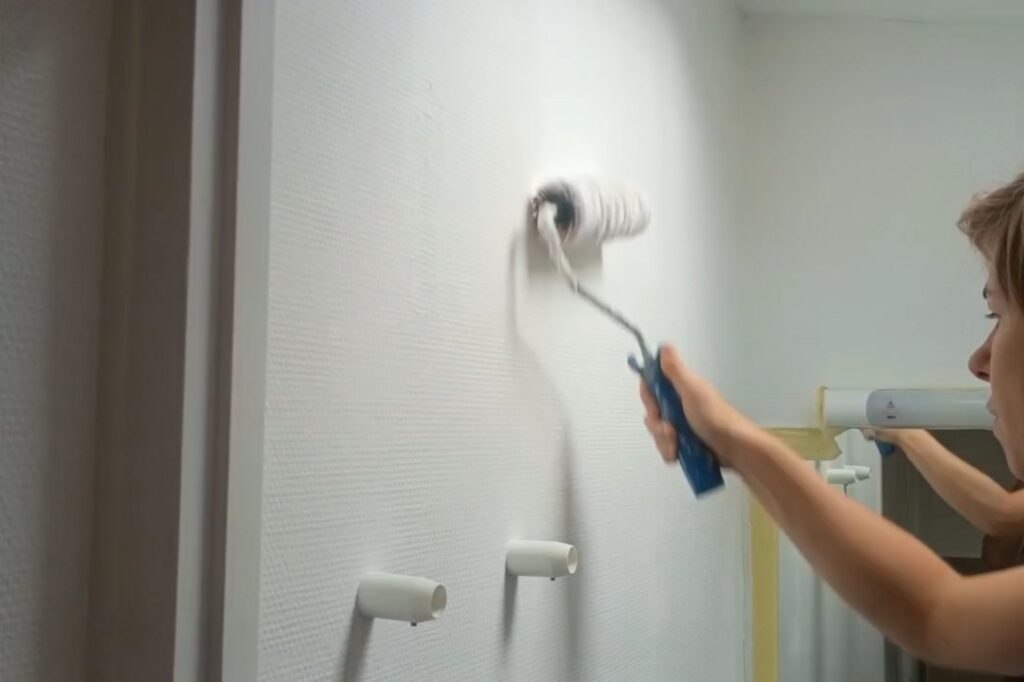 Application de peinture au rouleau sur le mur d’une salle de bain rénovée après un dégât des eaux