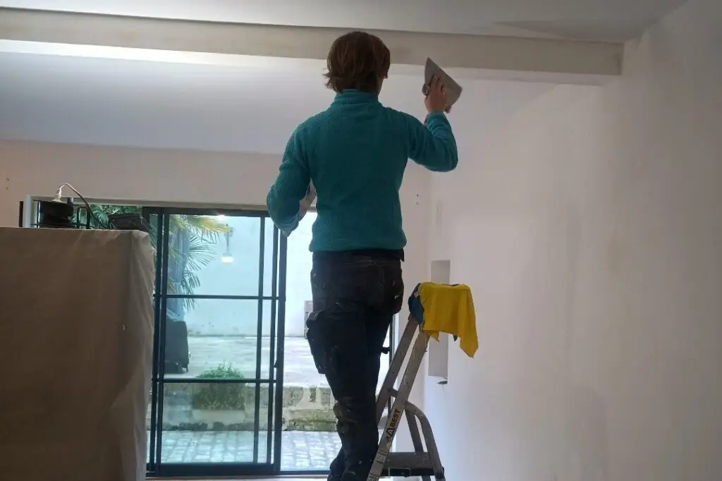 Artisan peintre à Rochefort en train d’enduire un mur avec des spatules pour préparer la surface avant peinture, lors d’une rénovation intérieure en Charente-Maritime.
