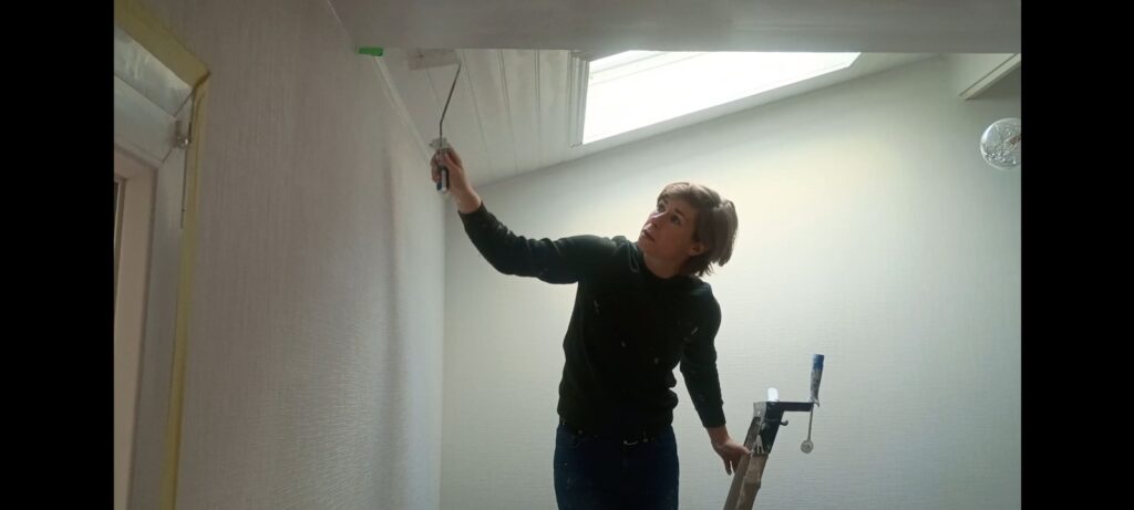 Artisan peintre qui peint du papier à peindre au rouleau télescopique pour une rénovation intérieure.