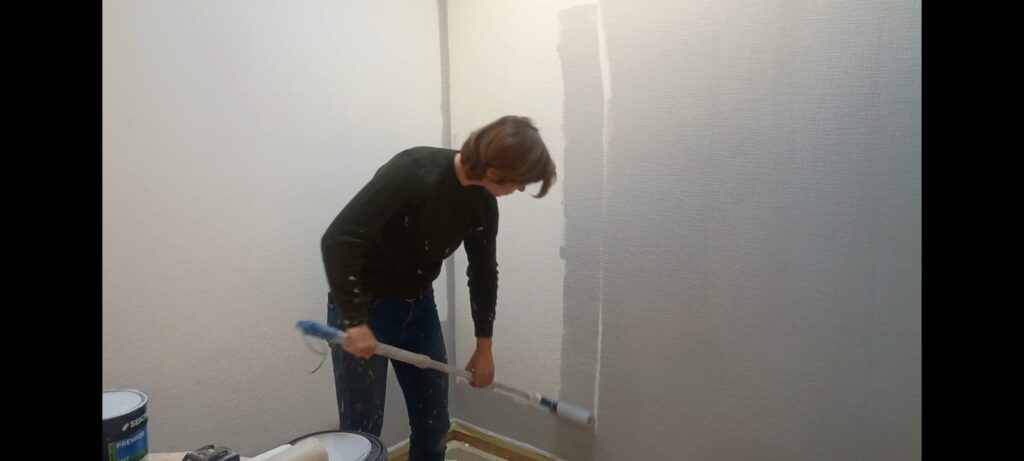 Artisan peintre rénovant un salon à Périgny en peignant du papier à peindre avec un rouleau monté sur perche.