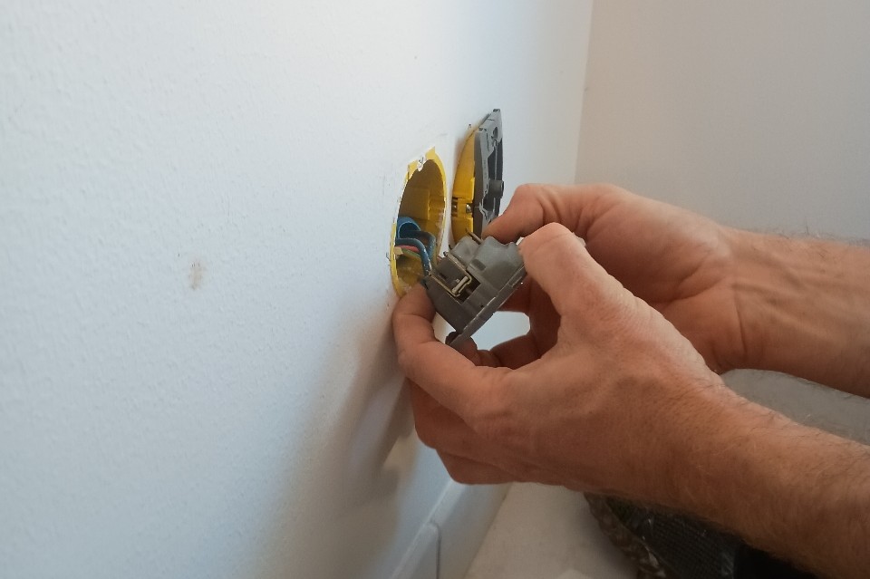 Mains d’un artisan changeant les coques de prises électriques pour la pose de radiateurs
