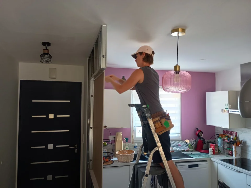 Artisan réalisant les finitions autour d'une verrière intérieure dans une cuisine